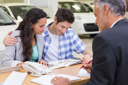 Smiling couple reading a booklet at new car showroom
