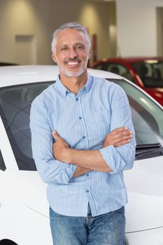 Smiling customer leaning on car with arms crossed at new car showroom