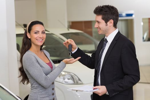 Smiling businessman giving car key to happy customer at new car showroom