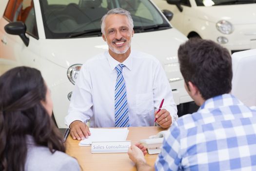 Salesman speaking with his clients at new car showroom