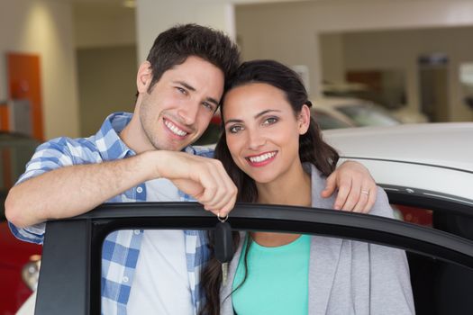Smiling couple holding their new car key at new car showroom