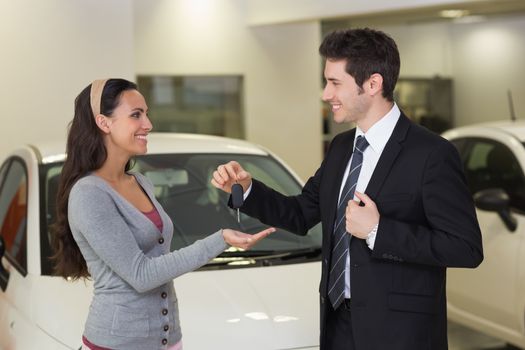 Smiling businessman giving car key to happy customer at new car showroom