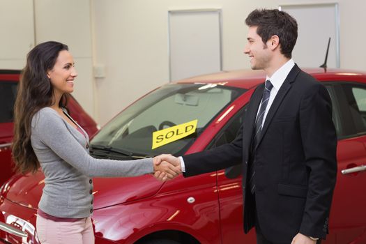 Person shaking hands in front of a sold car at new car showroom