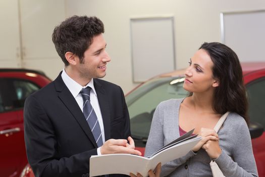 Smiling businessman speaking with his customer at new car showroom