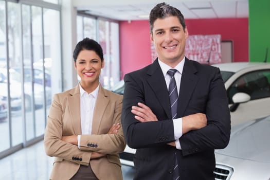 Smiling colleagues standing with arms crossed at new car showroom