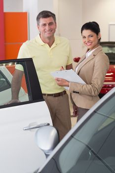 Businesswoman and her client smiling at camera at new car showroom