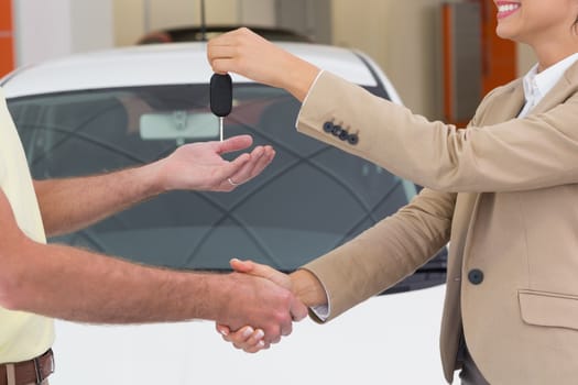 Businesswoman giving key while shaking a customer hand at new car showroom