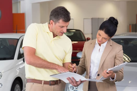 Salesperson talking with her customer while holding a booket at new car showroom