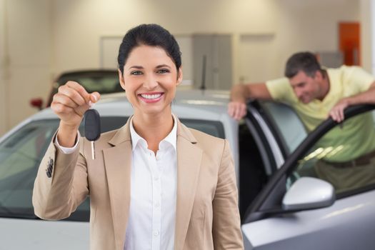 Smiling saleswoman showing a customer car key at new car showroom
