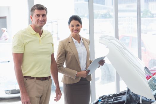 Businesswoman and customer looking at a car engine at new car showroom