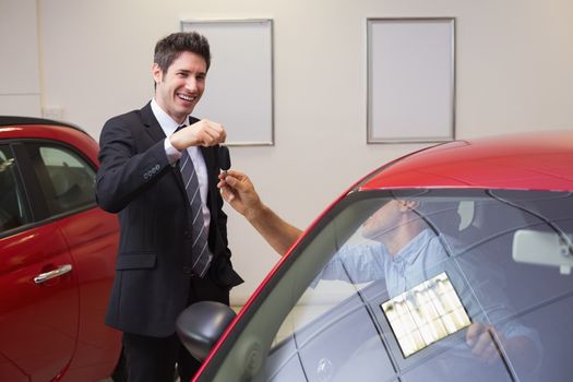 Businessman giving car key while shaking a customer hand at new car showroom