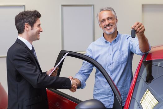 Customer showing his new key while shaking a hand at new car showroom