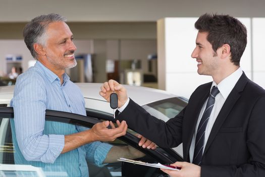 Smiling businessman giving car key to happy customer at new car showroom