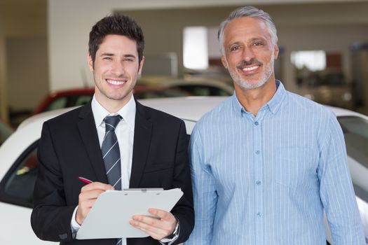 Smiling businessman writing on clipboard at new car showroom