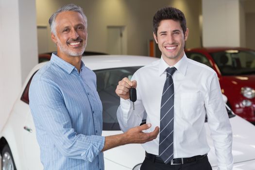 Smiling businessman giving car key to happy customer at new car showroom