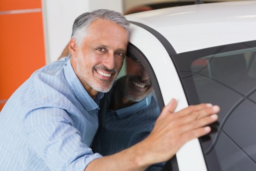 Smiling man hugging a white car at new car showroom