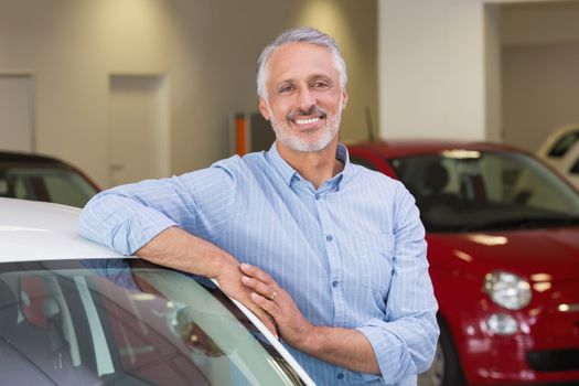 Smiling customer leaning on car at new car showroom