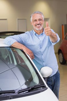 Smiling customer leaning on car while giving thumbs up at new car showroom