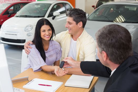 Salesman giving key to a smiling couple at new car showroom