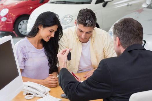 Smiling couple signing salesman contract at new car showroom