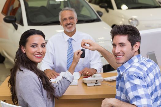 Smiling couple holding their new car key at new car showroom