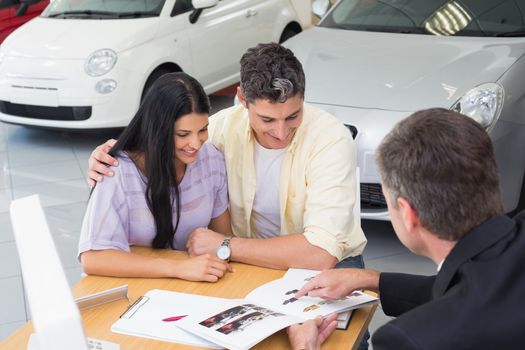 Salesperson pointing something on booklet at new car showroom