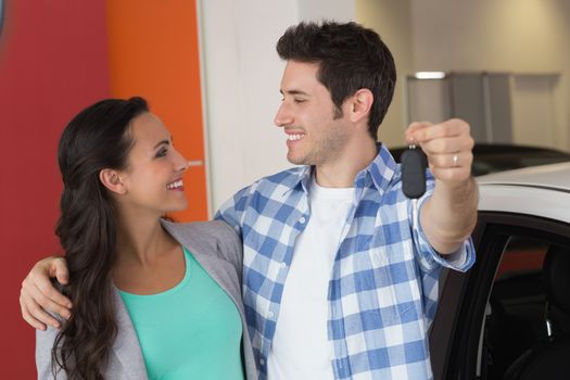 Smiling couple holding their new car key at new car showroom