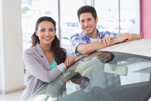 Smiling couple leaning on car at new car showroom