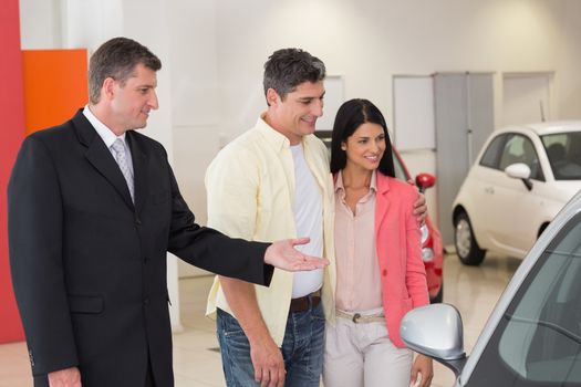 Smiling businessman presenting a car at new car showroom