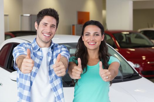 Smiling couple standing while giving thumbs up at new car showroom