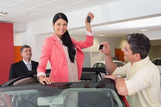 Woman standing in red cabriolet and man taking picture at new car showroom