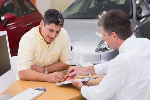 Salesman showing client where to sign the deal at new car showroom