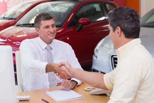 Smiling salesman shaking a customer hand at new car showroom