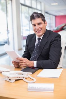 Smiling salesperson holding a document at new car showroom