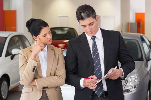 Business team working together on clipboard at new car showroom