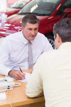 Smiling salesman writing on contract at new car showroom