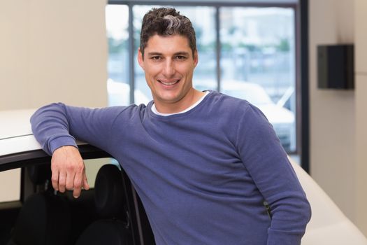 Smiling customer leaning on car at new car showroom