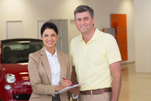 Smiling businesswoman speaking with her client at new car showroom