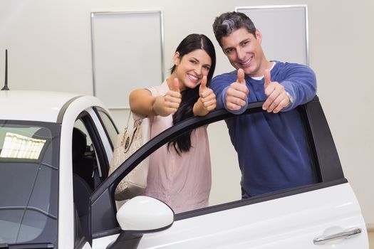 Smiling couple standing while giving thumbs up at new car showroom