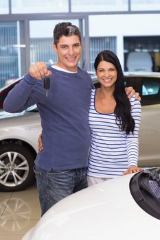 Smiling couple holding their new car key at new car showroom