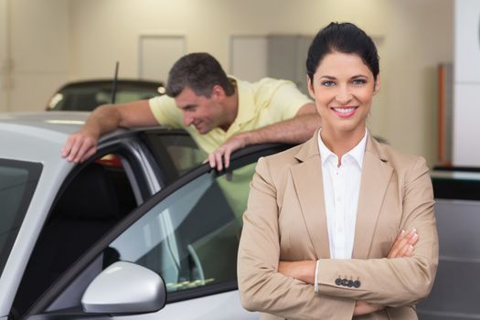 Smiling businesswoman standing with arms crossed at new car showroom