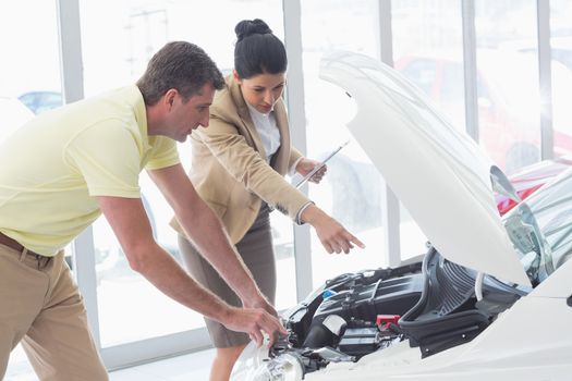 Businesswoman and customer looking at a car engine at new car showroom