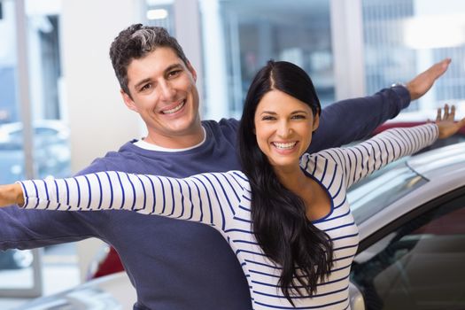 Happy couple standing with arms outstretched at new car showroom