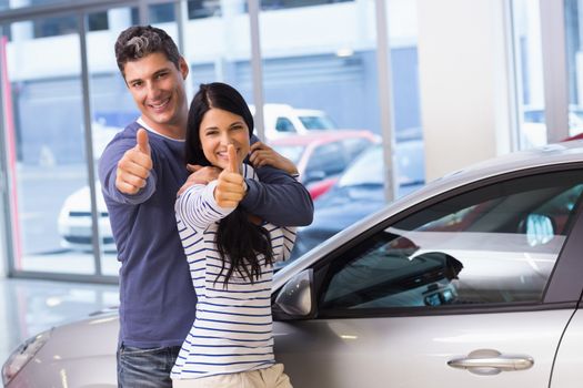 Smiling couple giving thumbs up at new car showroom