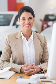 Happy businesswoman working at her desk at new car showroom