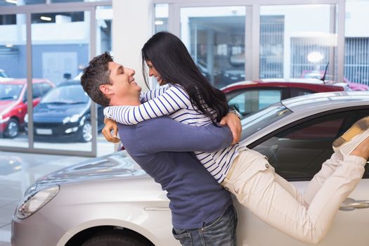 Smiling couple hugging and smiling at new car showroom