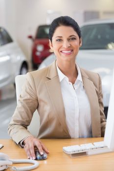Smiling businesswoman working in her desk at new car showroom