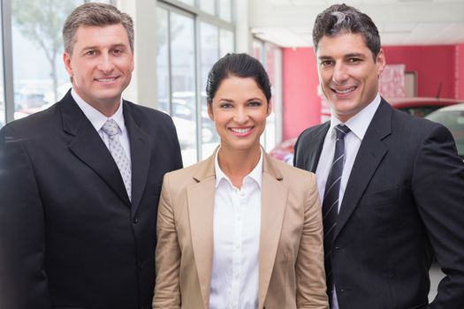 Group of smiling business team standing together at new car showroom