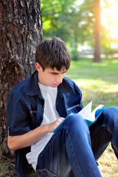 Serious Teenager with the Book under the Tree in the Summer Park