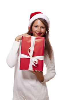 Pretty woman in a festive red Santa hat with a large matching red Christmas gift tied with a ribbon and bow holding it in front of her with a happy smile showing it to the camera, on white
